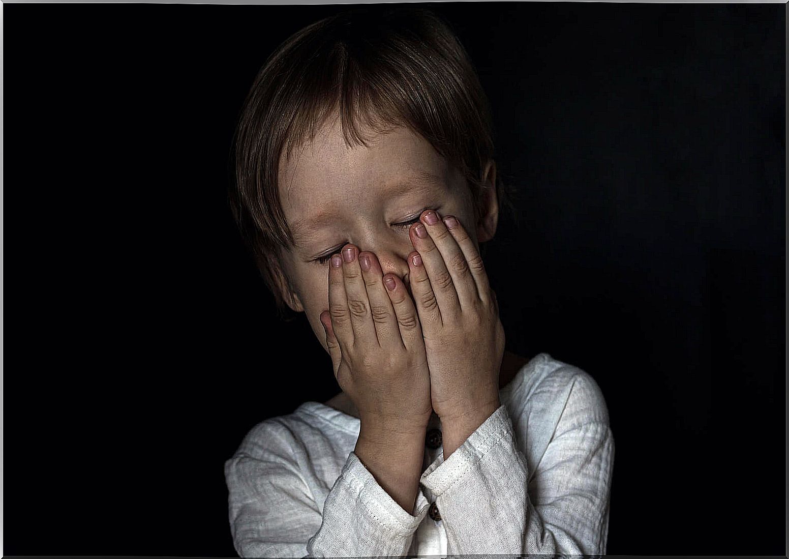 Child afraid of the dark covering his face with his hands.