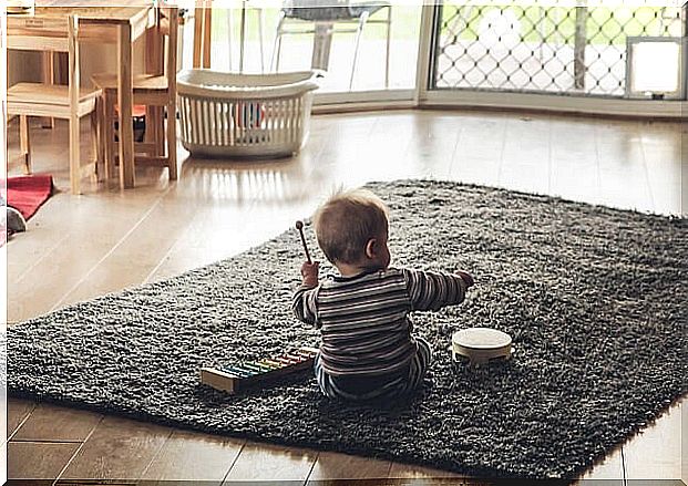 Baby sitting on a rug playing a xylophone and a tambourine.