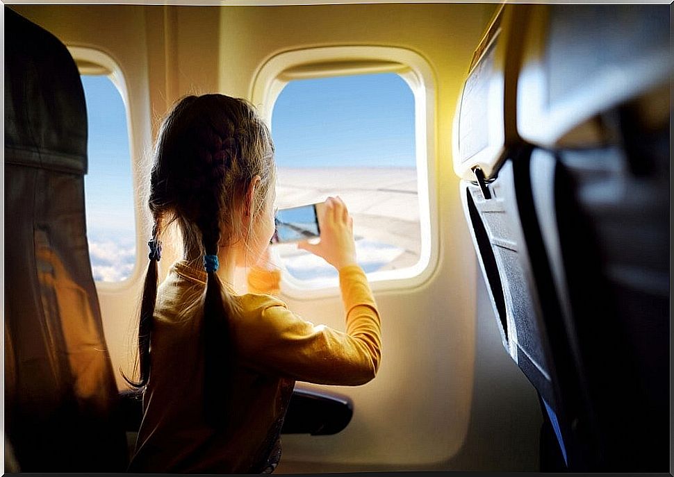 Children taking a photo with their mobile through the window of the plane on one of their vacation flights.